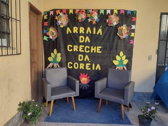 Painel “Arraiá da Creche da Coreia”, com chapéus de palha, fogueira de papel e duas poltronas para fotos