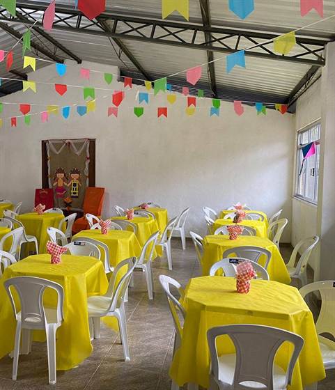 Salão decorado para o Arraiá da Creche, com bandeirinhas e mesas com toalhas amarelas