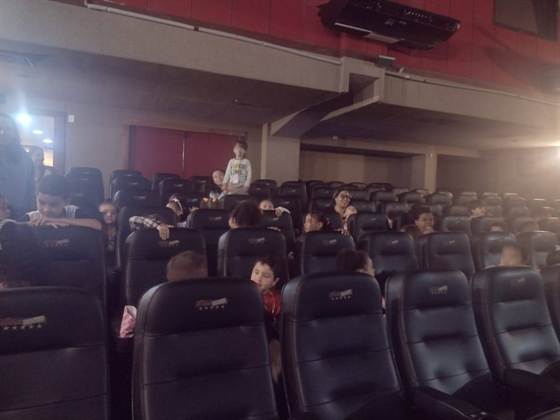 Crianças e acompanhantes nas poltronas da sala de cinema antes da sessão