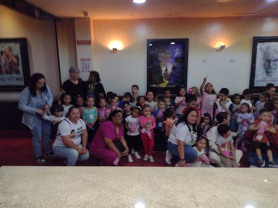 Turma posando para foto no saguão do cinema, em frente a cartazes de filmes