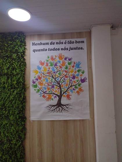 Cartaz com árvore de mãozinhas e a frase “Nenhum de nós é tão bom quanto todos nós juntos”