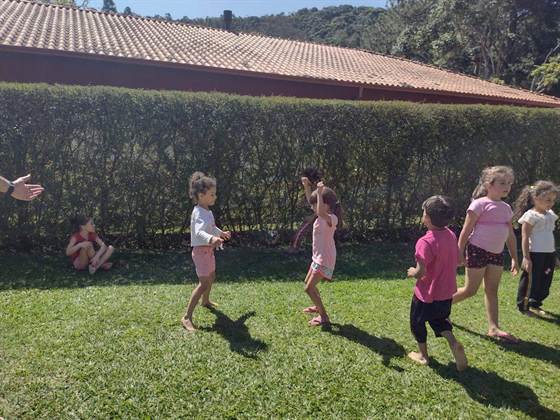 Crianças brincando em roda no gramado, cercadas por uma cerca viva